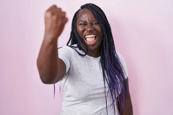 ピンク色の背景に立っている若いアフリカの女性は怒りで叫んでいる間 怒りと怒りに苛まれ 激しく拳を上げる 怒りと攻撃的な考え方 — ストック写真