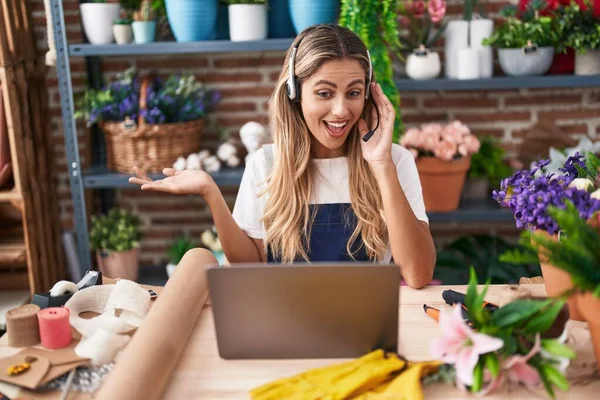 Young blonde woman working at florist shop doing video call celebrating achievement with happy smile and winner expression with raised hand