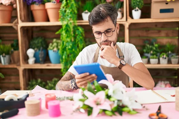Young hispanic man florist using touchpad with serious expression at flower shop