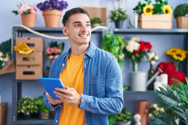 Young hispanic man florist smiling confident using touchpad at florist store