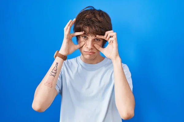 Hispanic Young Man Standing Blue Background Trying Open Eyes Fingers — Φωτογραφία Αρχείου