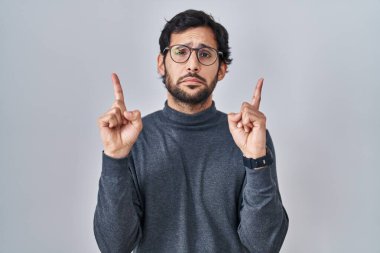 Yakışıklı Latin adam izole edilmiş arka planda dikiliyor üzgün ve üzgün görünüyor, parmaklarıyla yönü gösteriyor, mutsuz ve depresif.. 