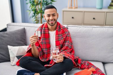 African american man taking pills sitting on sofa at home