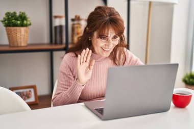 Orta yaşlı bir kadın evdeki masada video görüşmesi yapıyor.