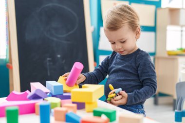 Anaokulundaki masada oturan sevimli sarışın çocuk geometri bloklarıyla oynuyor.