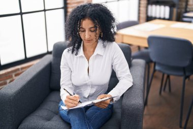 Young hispanic woman business worker writing on document at office