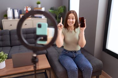 Güzel esmer kadın evde akıllı telefonuyla video kaydı yapıyor. Bir fikir ya da soruyla gülümsüyor ve mutlu yüzle işaret ediyor. 