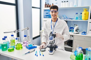 Laboratuvarda mikroskop kullanarak bilim adamı üniforması giyen genç bir İspanyol.