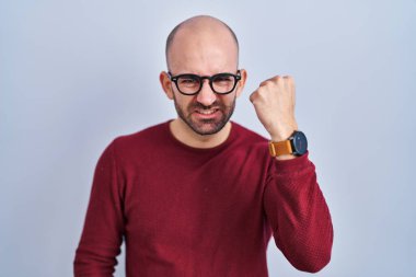 Beyaz arka planda sakallı genç bir adam kızgın ve kızgın gözlükler takıyor öfkeyle bağırırken yumruğunu kaldırıyor. öfke ve agresif konsept. 