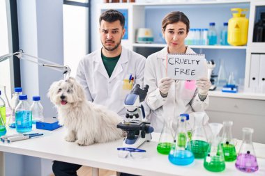 Young hispanic people working at scientist laboratory with dog skeptic and nervous, frowning upset because of problem. negative person. 