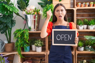 Çiçekçide çalışan genç İspanyol kadın elinde açık bir tabela tutuyordu. Öfkeyle bağırıyordu. Öfkeyle bağırıyordu. 