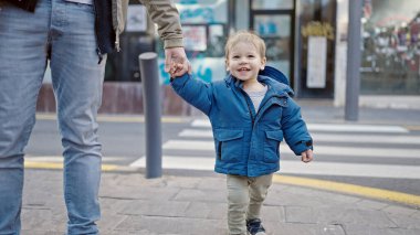 Beyaz çocuk sokakta babamla el ele tutuşurken gülümsüyor.