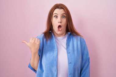 Pembe arka planda duran Latin kökenli genç bir kadın elleri yandan işaret ederek şaşırdı, ağzı açık şaşkın bir şekilde ifade etti.. 