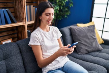 Evdeki kanepede oturan akıllı telefon kullanan genç, güzel İspanyol kadın.