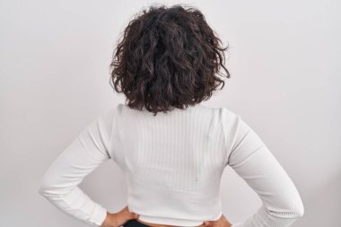 Kıvırcık saçlı İspanyol kadın izole bir arka planda duruyor geriye bakıyor kolları vücudunda. 