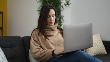 Güzel İspanyol kadın dizüstü bilgisayar kullanıyor. Evde endişeli bir ifadeyle oturuyor.