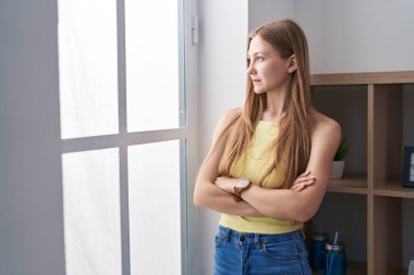 Young caucasian woman standing with arms crossed gesture and serious expression at home