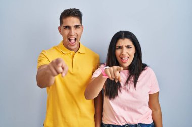 Young couple standing over isolated background pointing displeased and frustrated to the camera, angry and furious with you 