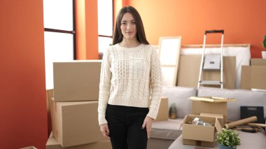 Genç, güzel, İspanyol bir kadın yeni evinde kendine gülerek duruyor.