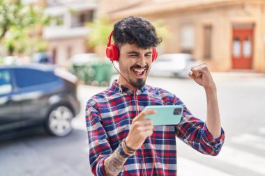 Young hispanic man smiling confident playing video game at street