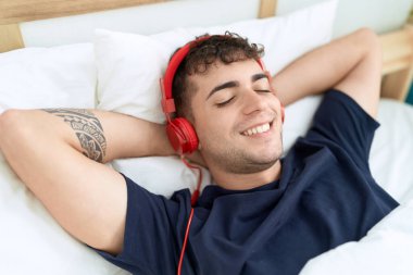 Genç İspanyol adam yatak odasında müzik dinliyor.