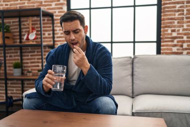 Genç İspanyol adam evdeki kanepede oturup hap alıyor.