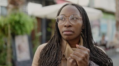 African woman standing with serious expression wearing glasses at street