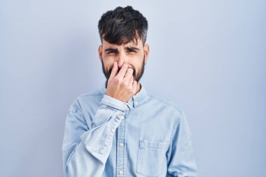Mavi arka planda dikilen sakallı genç bir İspanyol pis ve iğrenç bir koku alıyor. Nefesini burnunda tutuyor. Kötü kokuyor. 