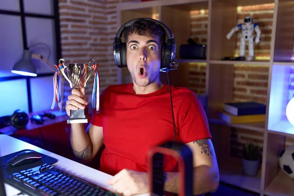 Young Hispanic Man Playing Video Games Holding Trophy Scared Amazed — Stock Photo, Image