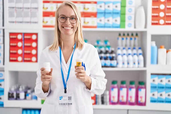 Young Blonde Woman Pharmacist Smiling Confident Holding Pills Bottles Pharmacy — Stok fotoğraf