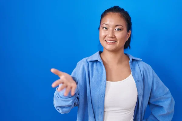 青い背景の上に立つアジアの若い女性が明るい笑顔でヤシの手を提供援助と受け入れ — ストック写真