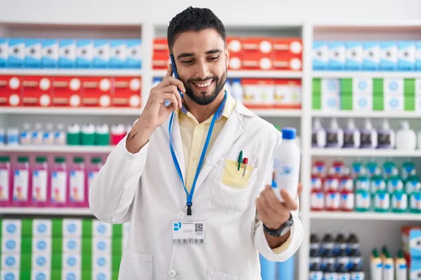 Jovem Árabe Homem Farmacêutico Segurando Garrafa Medicação Falando Smartphone Farmácia — Fotografia de Stock