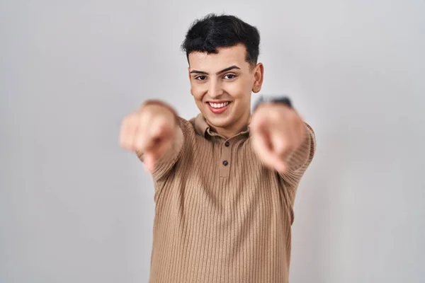 Non binary person standing over isolated background pointing to you and the camera with fingers, smiling positive and cheerful