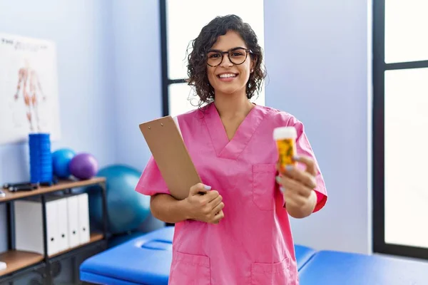 Young Latin Woman Wearing Physiotherapist Uniform Holding Pills Clinic — Φωτογραφία Αρχείου