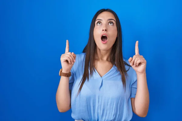 Young Brunette Woman Standing Blue Background Amazed Surprised Looking Pointing — Stock Photo, Image