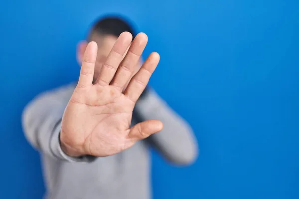 Stock image Hispanic man standing over blue background covering eyes with hands and doing stop gesture with sad and fear expression. embarrassed and negative concept. 