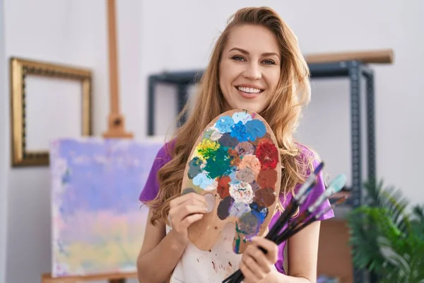 年轻的金发女艺术家微笑着 自信地在艺术工作室拿着画笔和调色板 — 图库照片