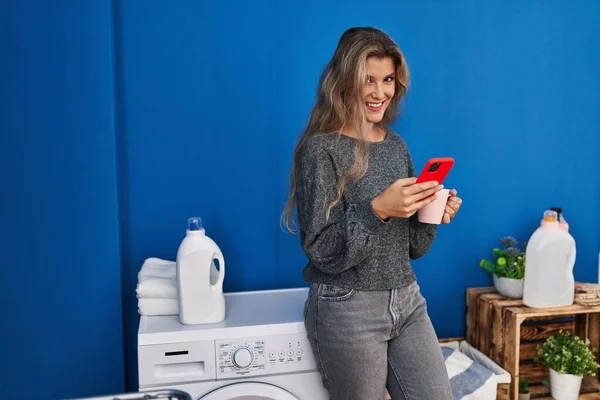 Akıllı Telefon Kullanan Kahve Içen Genç Sarışın Kadın Çamaşır Odasında — Stok fotoğraf