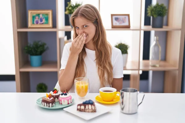 Młoda Biała Kobieta Jedząca Ciastka Śniadanie Wąchająca Coś Śmierdzącego Obrzydliwego — Zdjęcie stockowe