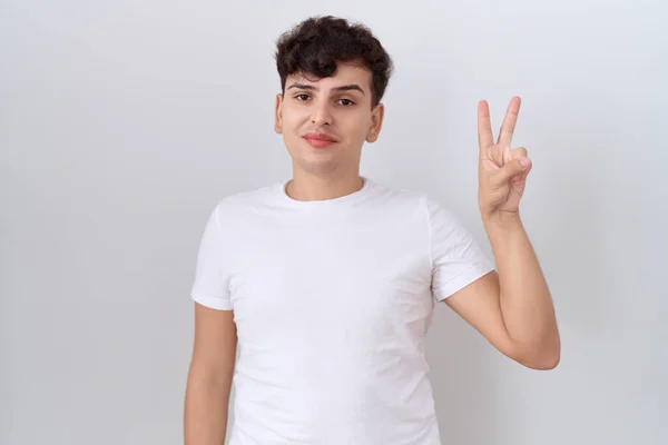 年轻的非二元男人穿着随意的白色T恤 手指点点2号 面带微笑 自信而快乐 — 图库照片