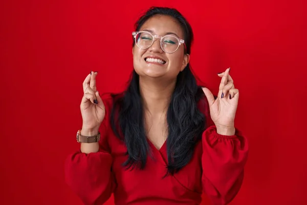 Azjatka Młoda Kobieta Stojąca Nad Czerwonym Tłem Gestykulująca Palcami Skrzyżowana — Zdjęcie stockowe