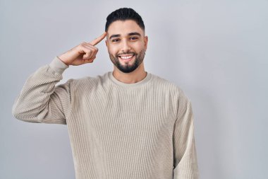 Soyutlanmış arka planda duran yakışıklı genç adam gülümseyerek tek parmağıyla kafasını işaret ediyor, harika bir fikir ya da düşünce, iyi bir hafıza. 