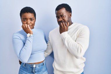 Mavi arka planda dikilen genç Afro-Amerikan çift elleri ağızlarında çivi yerken gergin ve stresli görünüyorlar. anksiyete. 