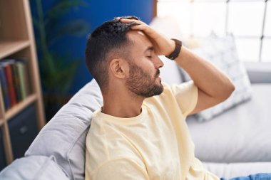 Young hispanic man stressed sitting on sofa at home