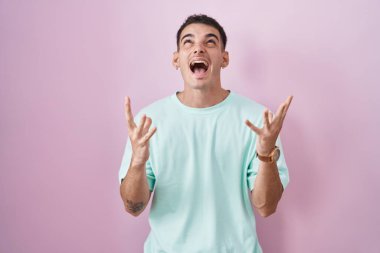 Yakışıklı İspanyol bir adam pembe arka planda duruyor deli gibi bağırıyor ve bağırıyor agresif bir ifade ve kollar havada. hüsran kavramı. 