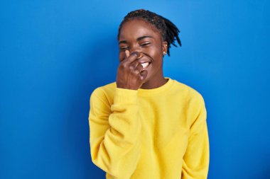 Güzel, siyah bir kadın mavi arka planda duruyor. Pis ve iğrenç bir koku alıyor. Nefesini burnunda tutuyor. Kötü kokuyor. 