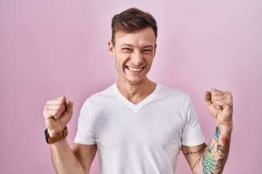 Pembe arka planda duran beyaz adam, kolları havada ve gözleri kapalı bir şekilde başarıyı kutluyor ve şaşırıyor. Kazanan konsept. 