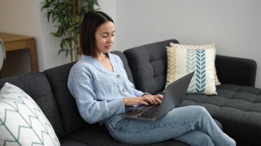 Evdeki kanepede dizüstü bilgisayar kullanan güzel İspanyol kadın.