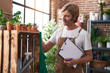 Çiçekçide kendine güvenen, güler yüzlü, sarışın bir adam.
