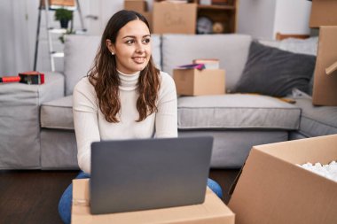 Young beautiful hispanic woman smiling confident using laptop at new home